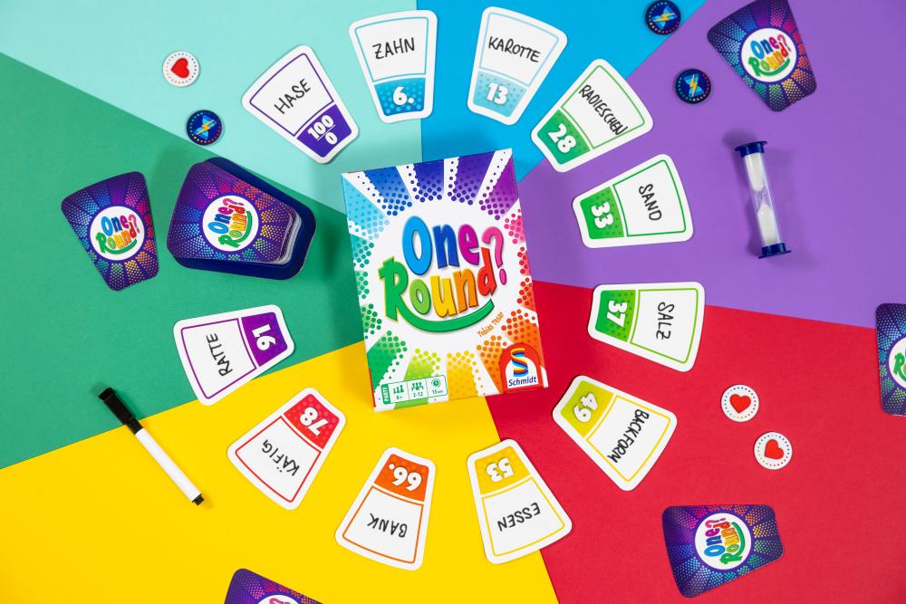 Buntes Kartenspiel One Round? mit Spielkarten, Sanduhr und Schachtel auf farbigem Untergrund.