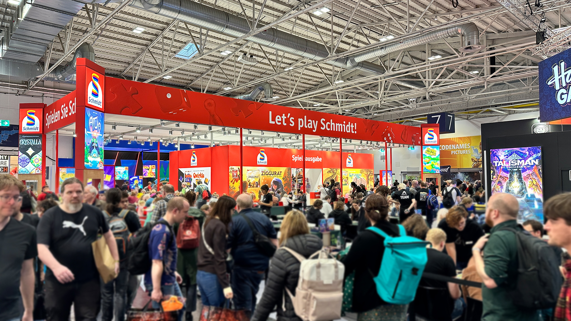 Messestand von Schmidt Spiele mit roten W&auml;nden, Spielzeugauslagen und mehreren Besuchern.
