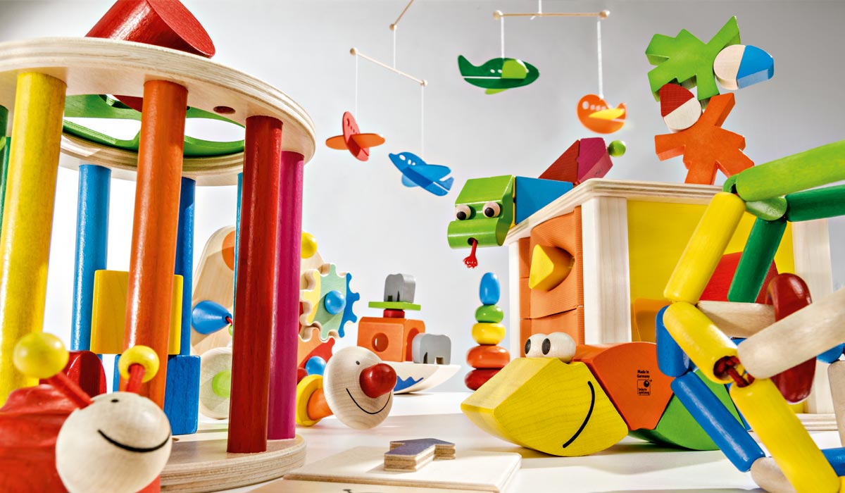 Bunte Holzspielzeuge: Rassel, Bausteine, Figuren und ein Mobile mit Flugzeugen und Fischen auf weißem Hintergrund.